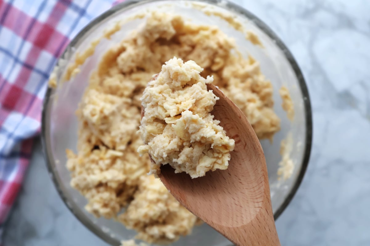 A close up of mixed potato chip cookie dough on a wooden spoon. The contents of the bowl full of dough is blurred in the background.