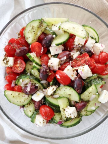 Final mixed Greek salad with chopped cucumbers, tomatoes, red onions, feta, and olives tossed in lemon oregano dressing.