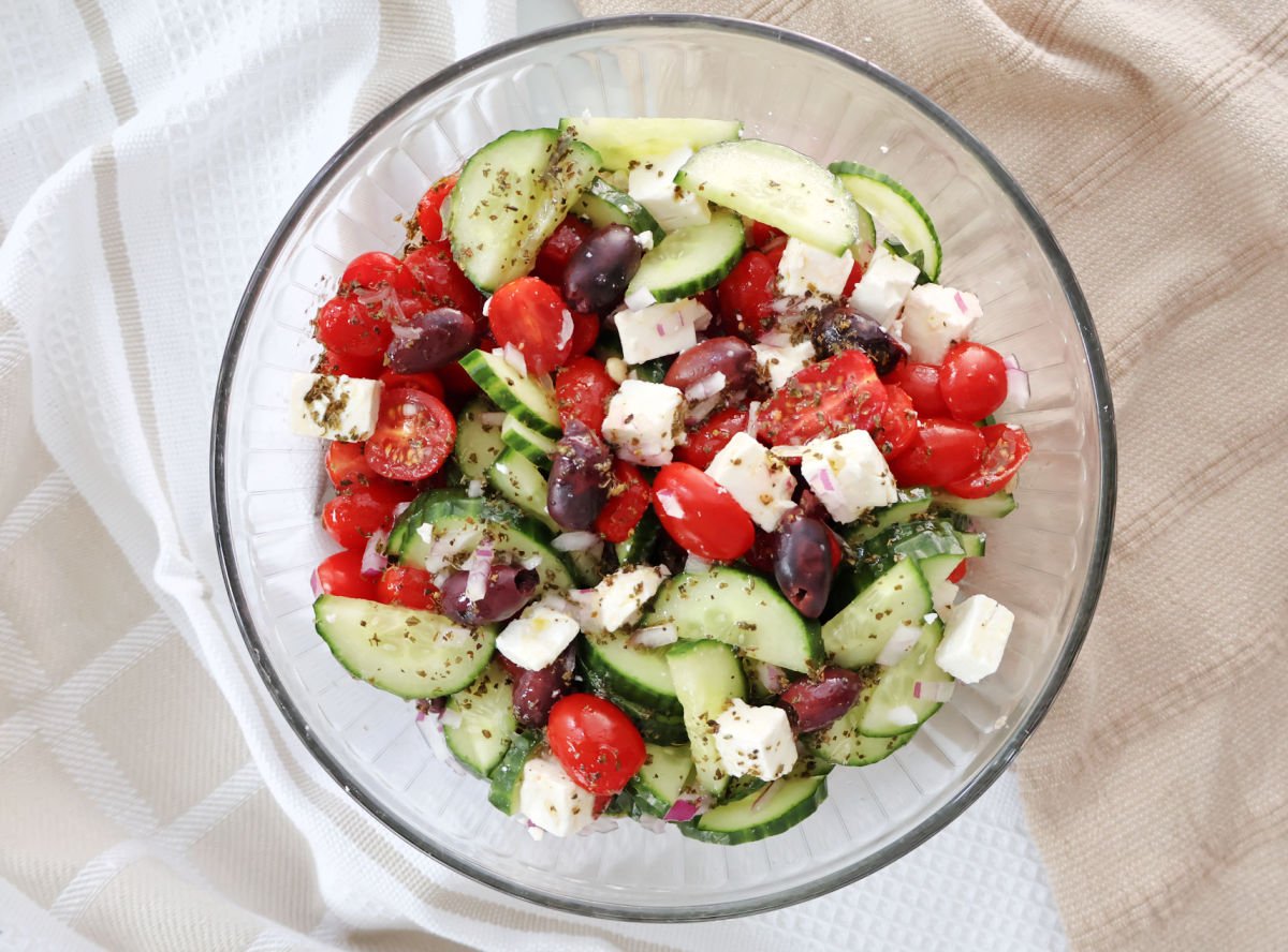Final mixed Greek salad with chopped cucumbers, tomatoes, red onions, feta, and olives tossed in lemon oregano dressing.