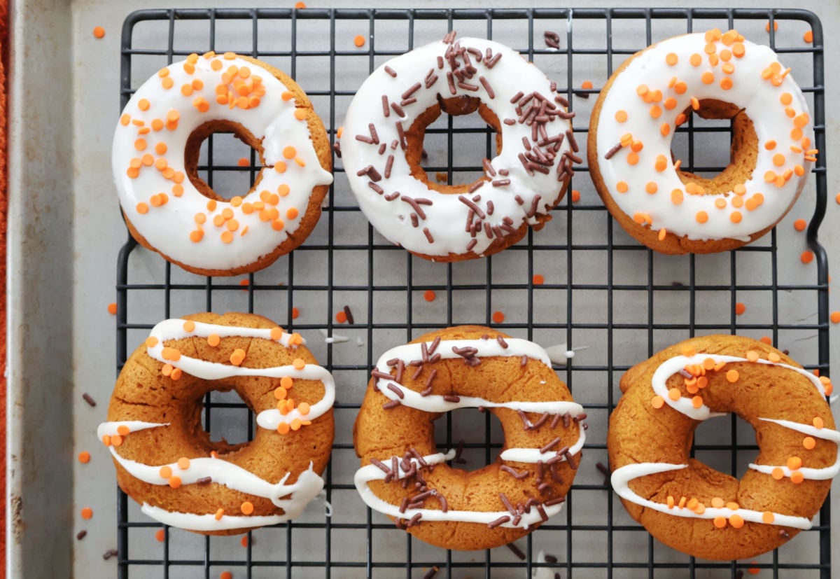 Golden brown baked pumpkin donuts on a cooling rack with icing drizzle and sprinkles.