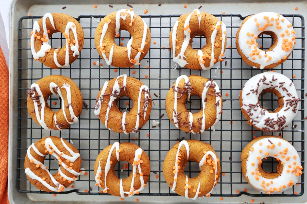 Golden brown baked pumpkin donuts on a cooling rack with icing drizzle and sprinkles.