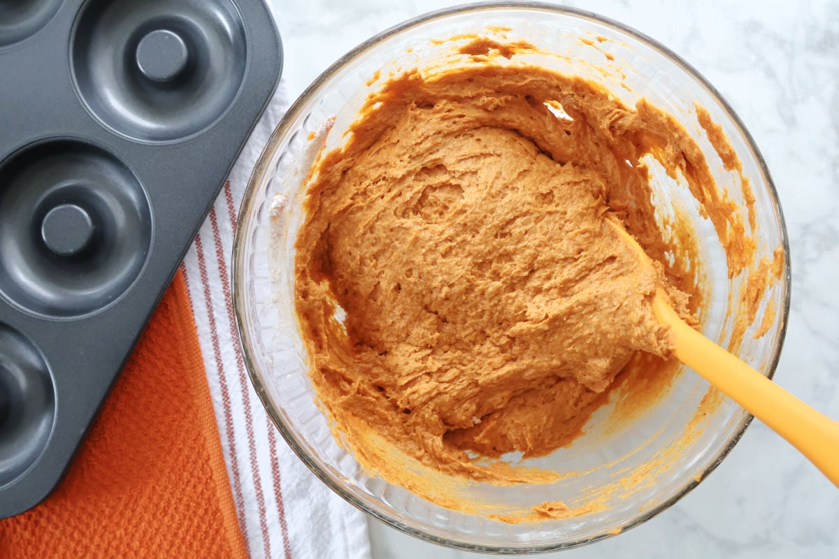 3 ingredient pumpkin spice donut batter in a glass bowl. Donut tin is beside the bowl.