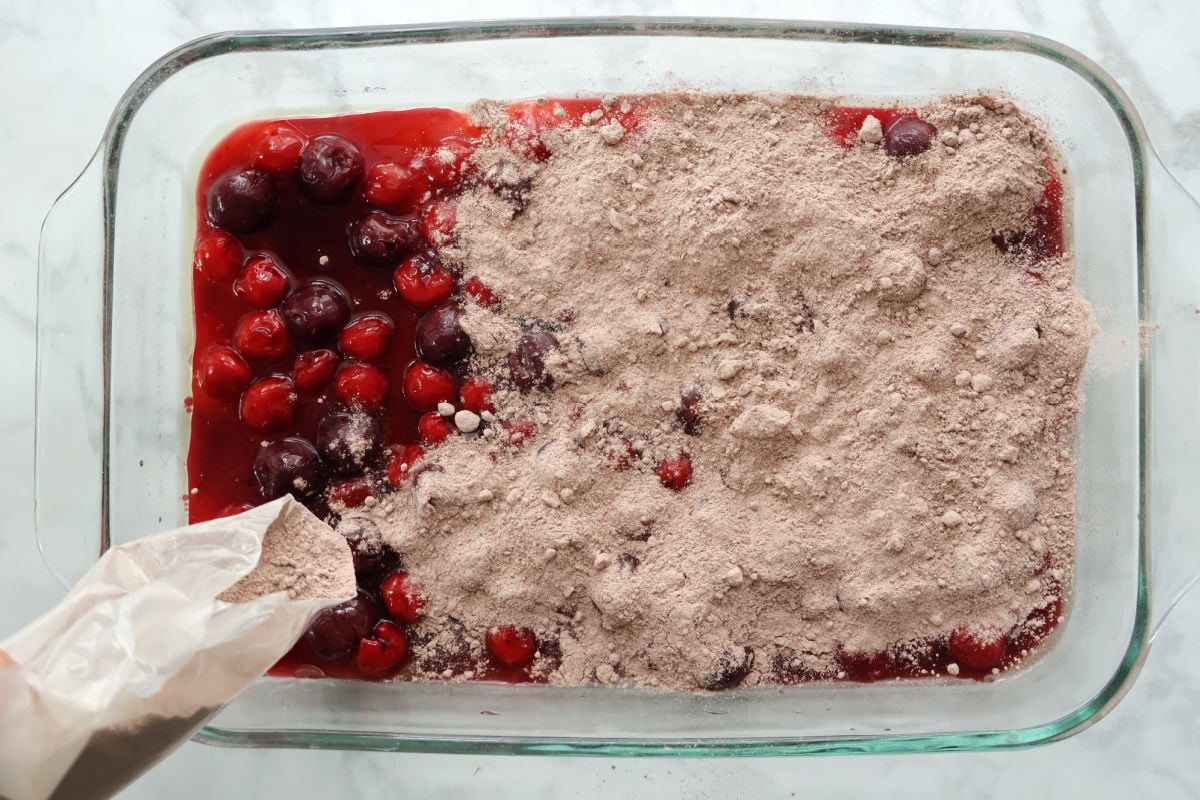 cake mix being evenly spread over canned cherries in a baking dish.