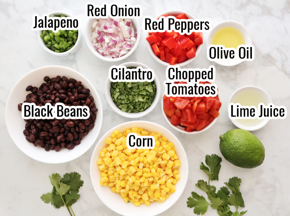Ingredients for black bean and corn salsa laid out on a kitchen counter including canned beans, corn, tomato, onion, and lime