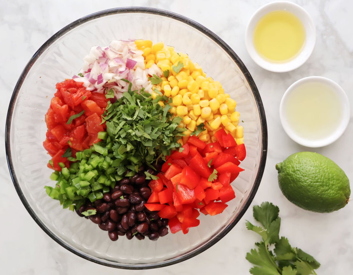 Black beans, corn, diced tomatoes, and red onion in a glass mixing bowl before tossing with dressing