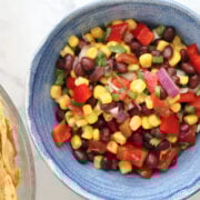 Black beans, corn, diced tomatoes, and red onion in a blue serving bowl after tossing with dressing. Corn tortilla chips are in a bowl to the side.