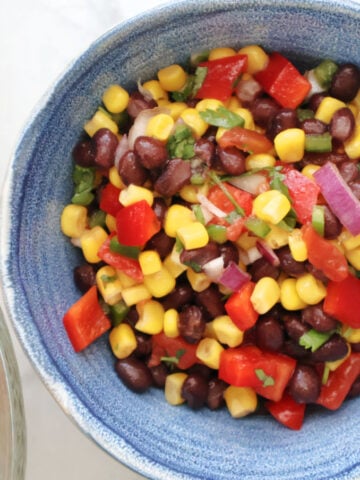 Black beans, corn, diced tomatoes, and red onion in a blue serving bowl after tossing with dressing. Corn tortilla chips are in a bowl to the side.