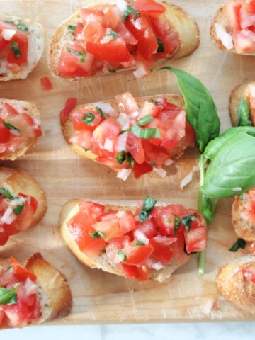 Overhead shot of toasted baguette slices topped with tomato basil bruschetta on a wooden serving board