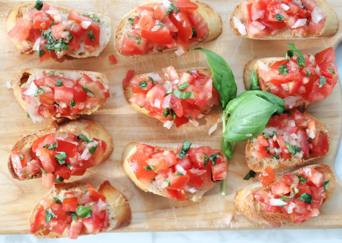 Overhead shot of toasted baguette slices topped with tomato basil bruschetta on a wooden serving board