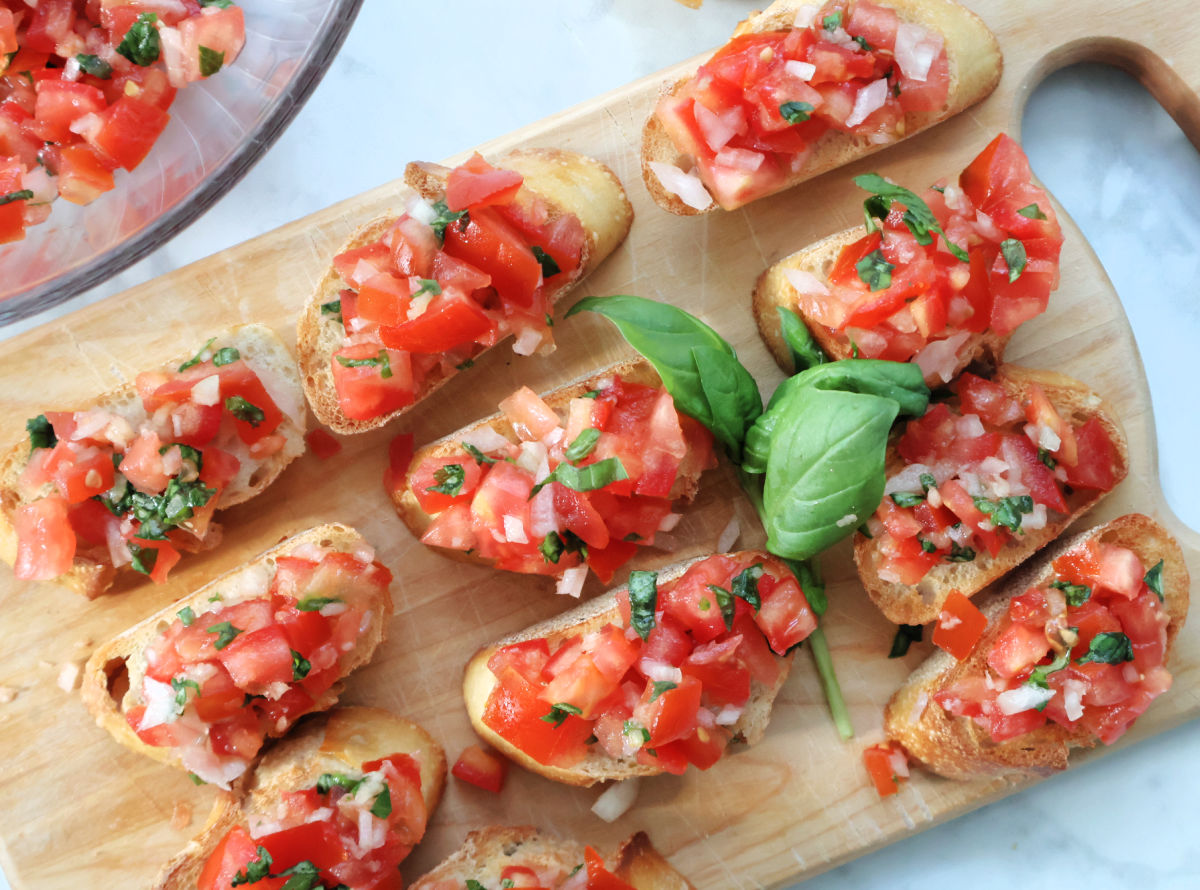 Overhead shot of toasted baguette slices topped with tomato basil bruschetta on a wooden serving board