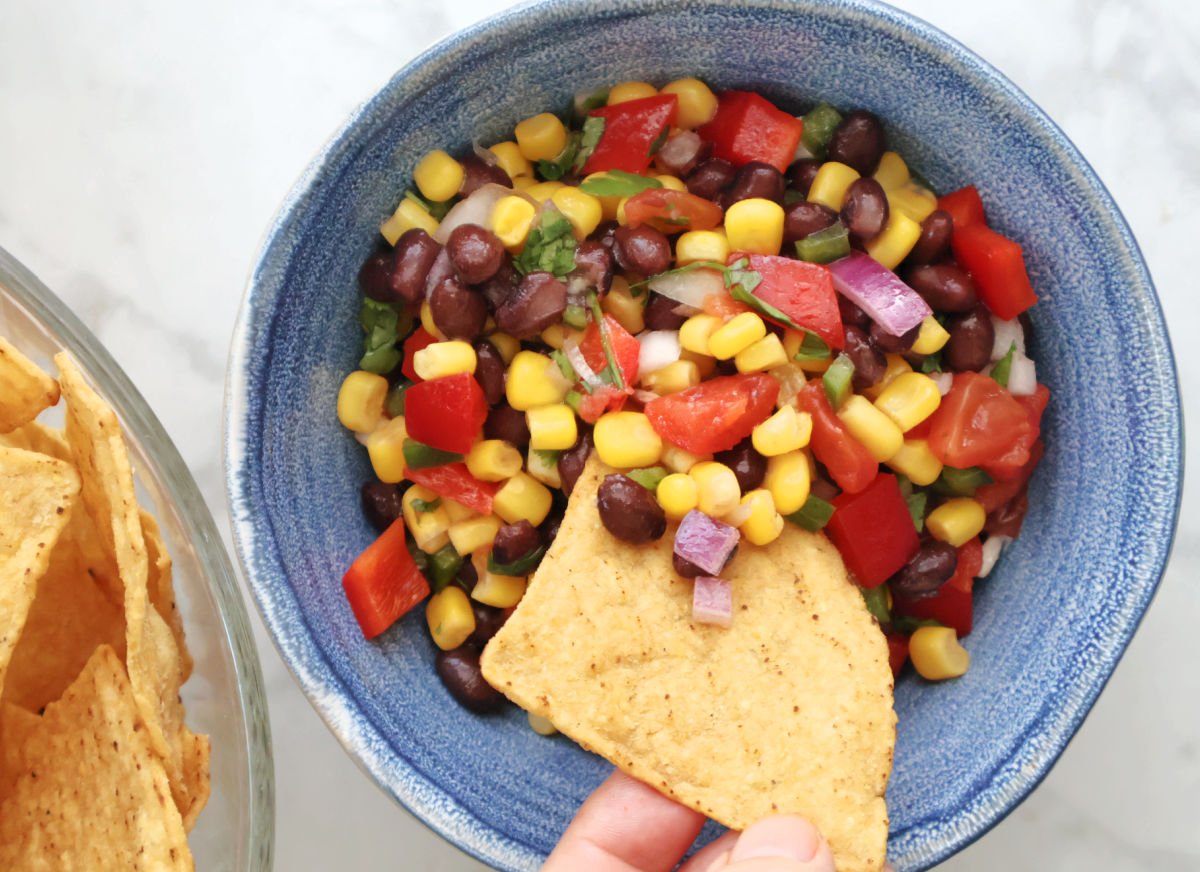 Close-up of tortilla chip holding black bean and corn salsa above the serving bowl, highlighting fresh ingredients