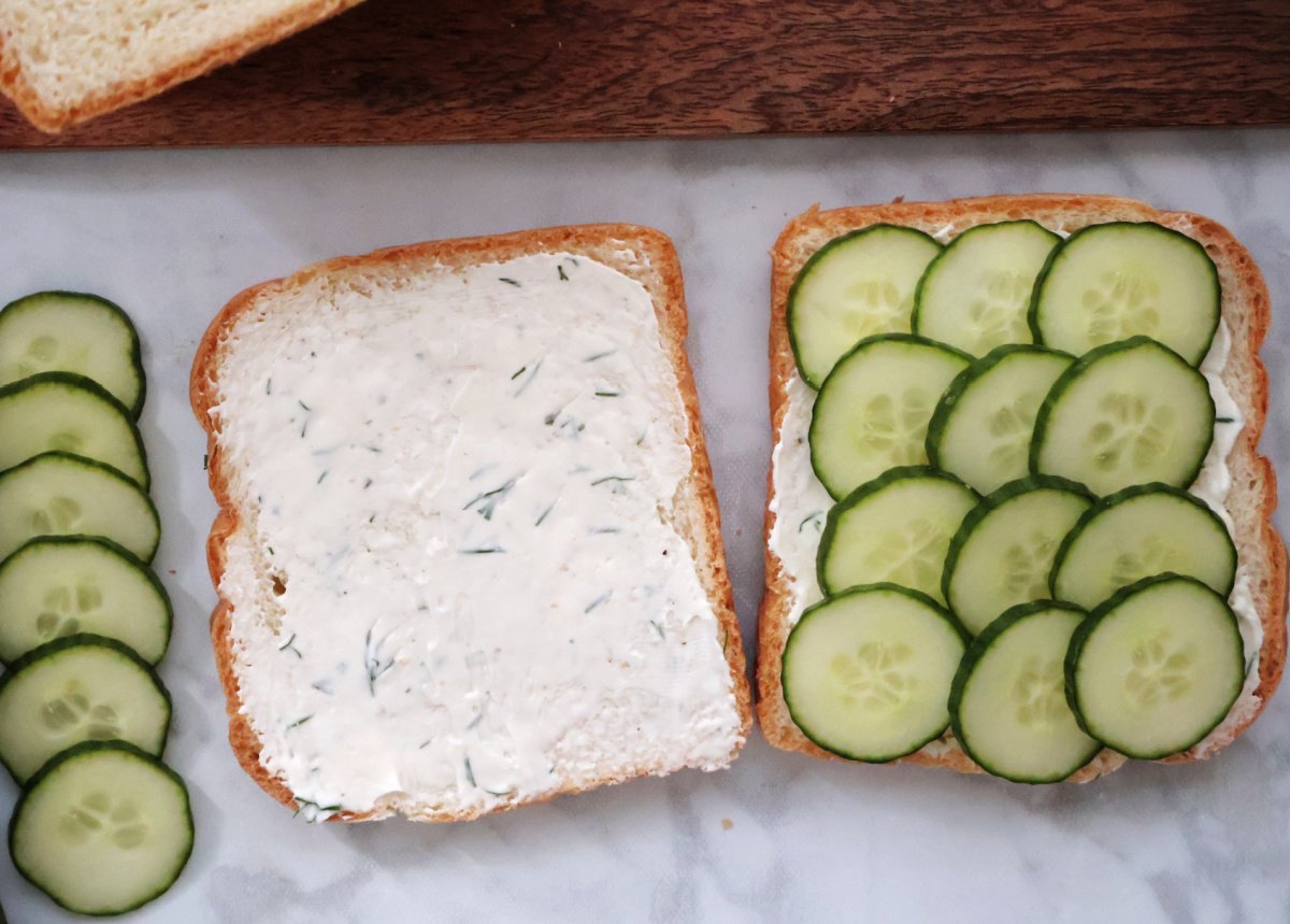 Preparing cucumber sandwiches with cream cheese spread and sliced cucumbers