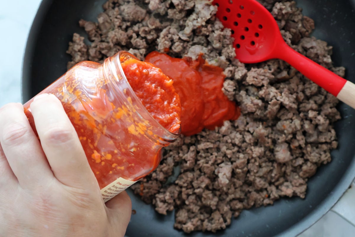 adding marinara sauce to ground beef and sausage crumbles.