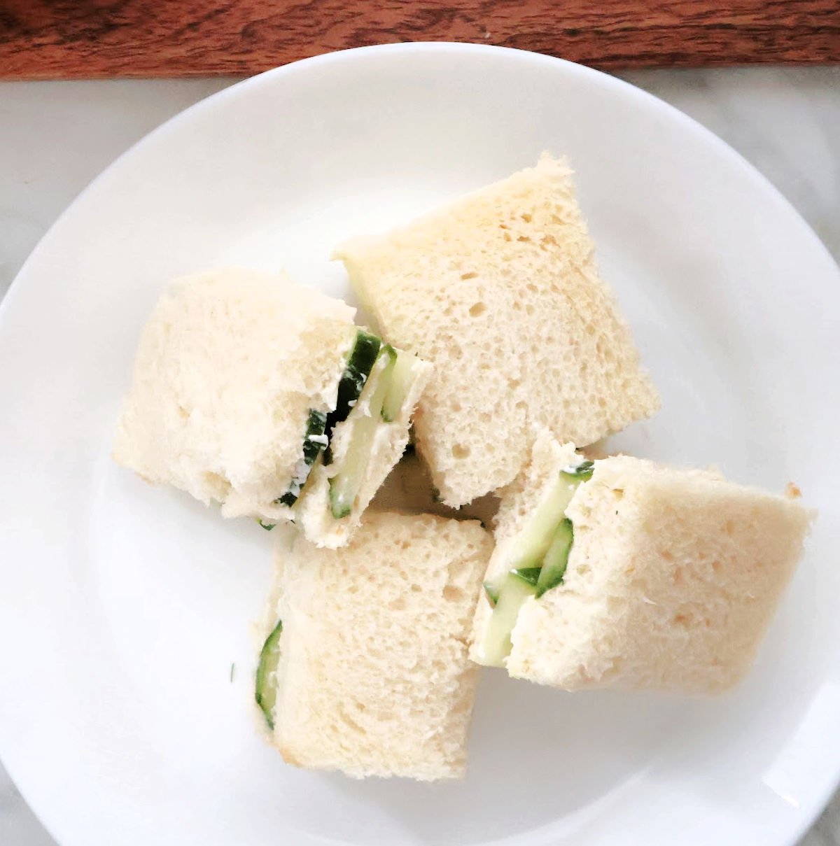 Cucumber sandwiches arranged on white plate with crusts removed