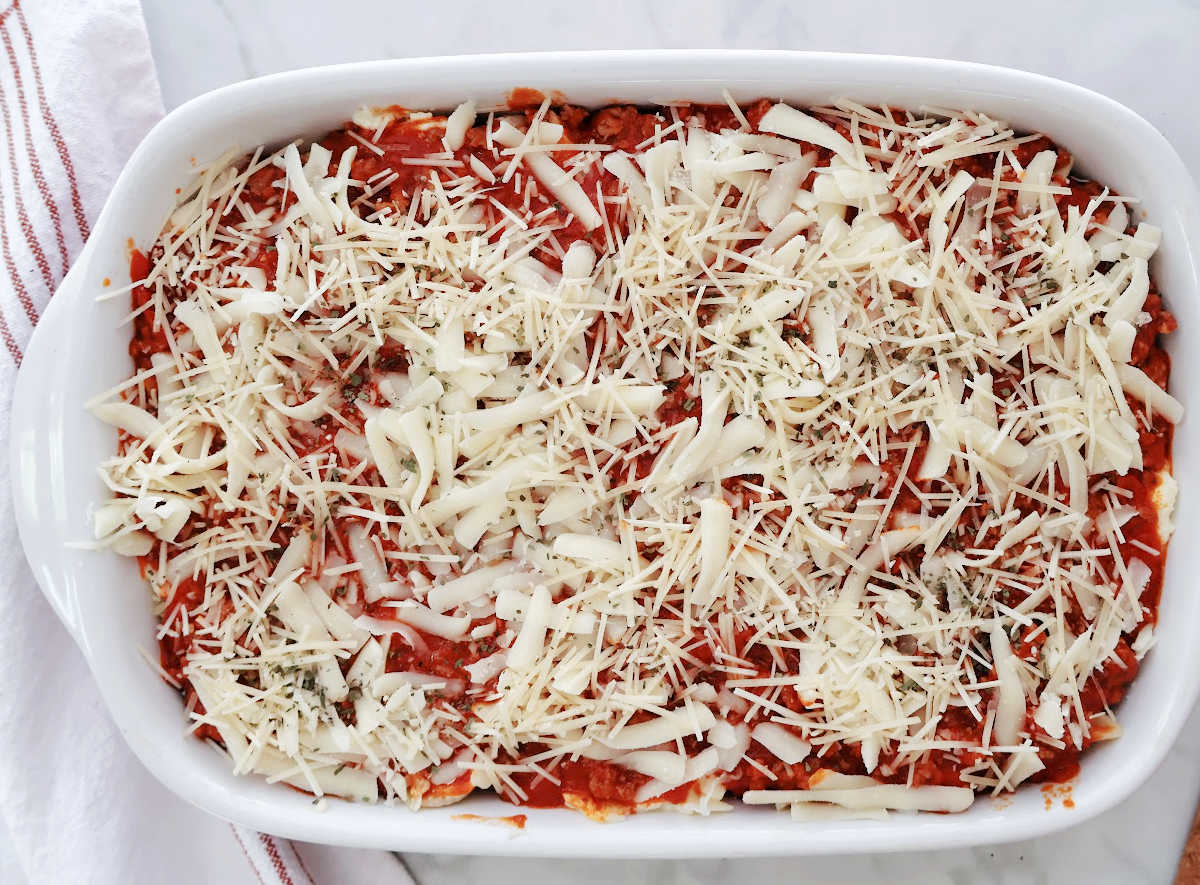 baked ziti with sausage ready for the oven. A delicious layer of mozzarella and parmesan cheese with a sprinkle of italian herbs on top.