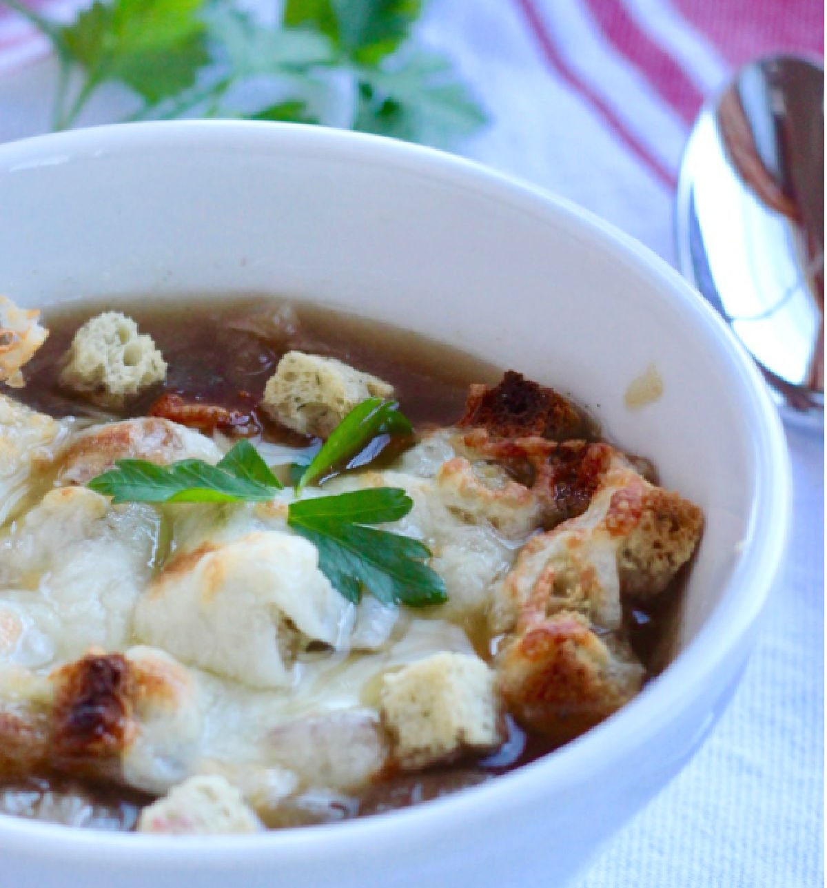 A bowl of french onion soup with croutons, melted cheese and parsley for garnish.