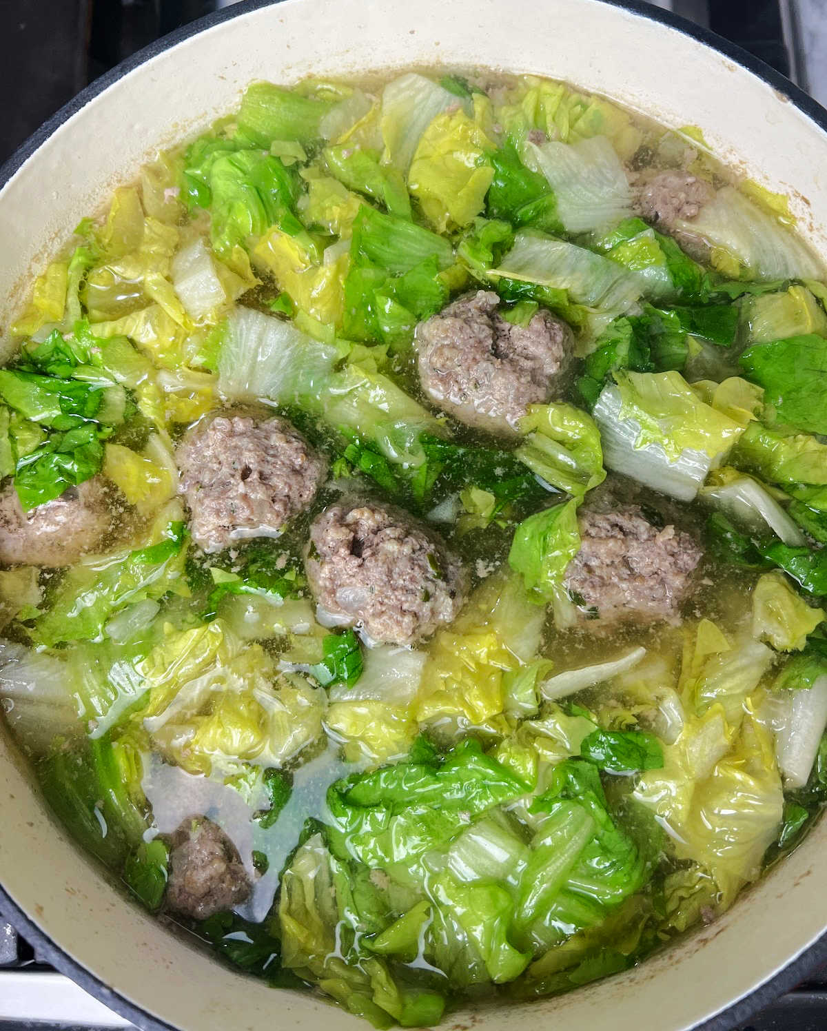 Italian wedding soup with escarole lettuce, chicken broth and meatballs,