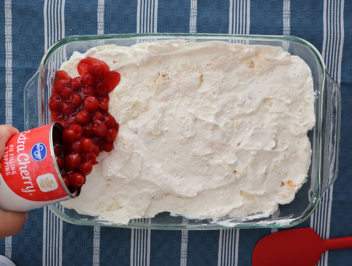 adding cherry pie filling onto fluffy white whipped cream and cream cheese and angel food cake layer.