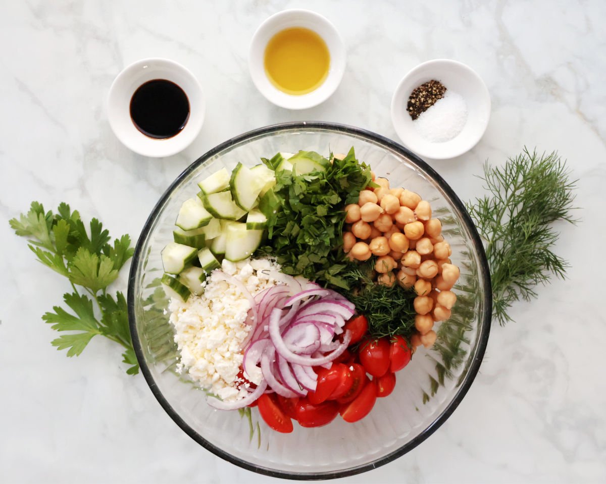Chopped cucumbers, tomatoes, and red onion with chick peas, parsley, dill , and feta in a prep bowl