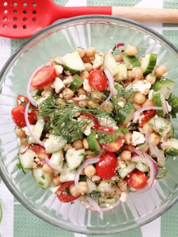Cucumber chickpea salad garnished with fresh dill and parsley sprigs