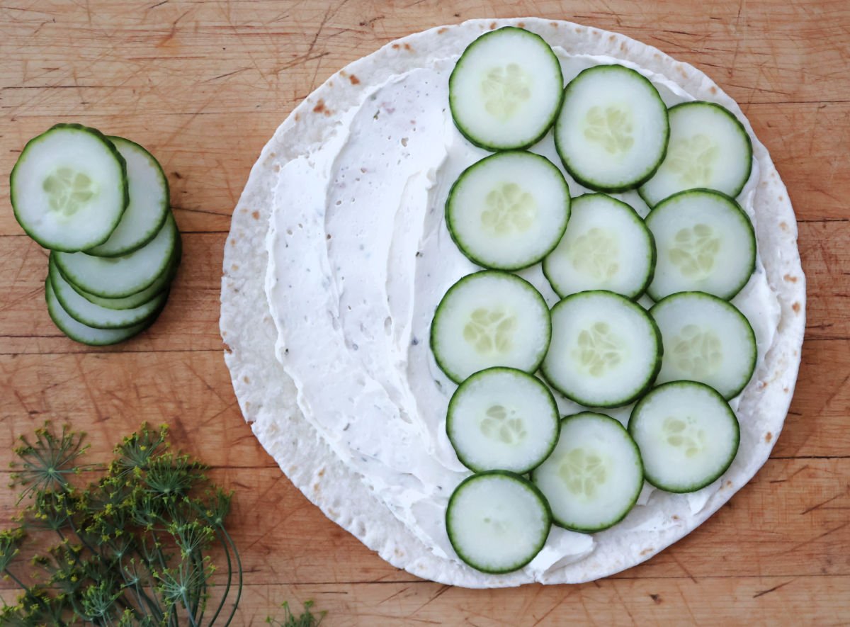 cucumbers being spread on the cream cheese and ranch layer on the tortilla. Ready to roll up the cucumber pinwheels.