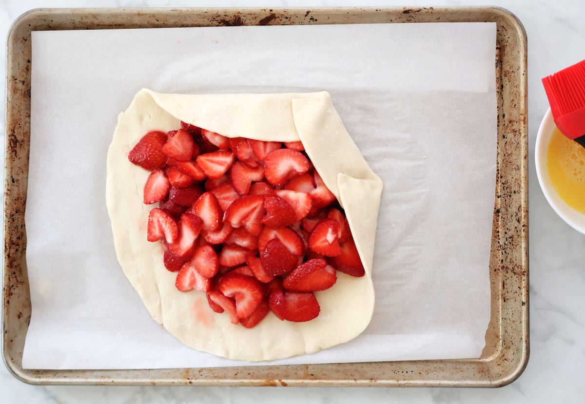 Strawberries in a pie crust being folded to create a rustic strawberry galette.