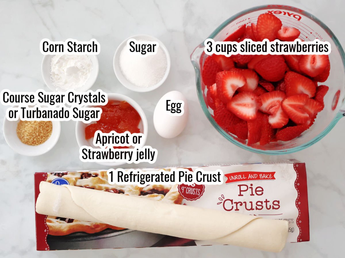 Strawberry galette ingredients including sliced strawberries, refrigerated pie crust, corn starch, sugar, course sugar crystals, an egg and jelly for the glaze.