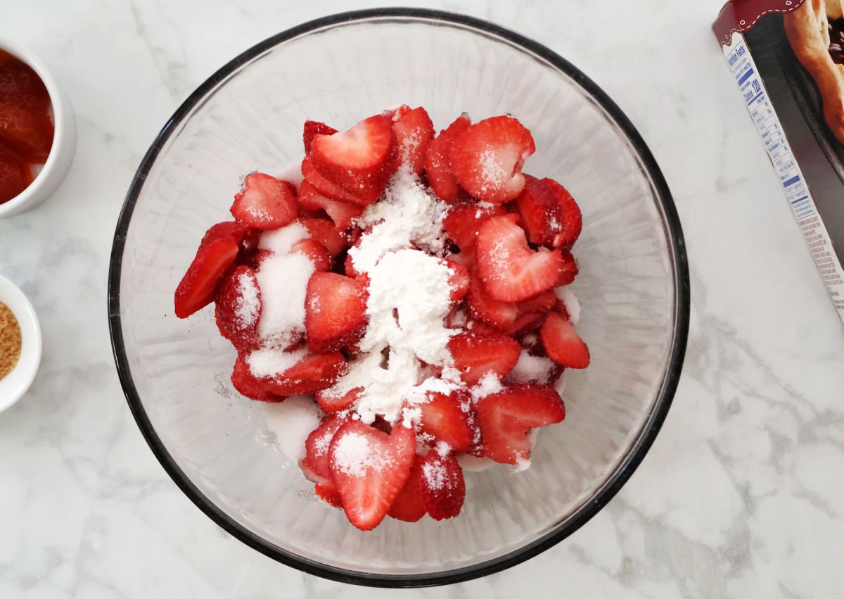 Fresh sliced strawberries with granulated sugar and cornstarch on top, ready to be mixed.