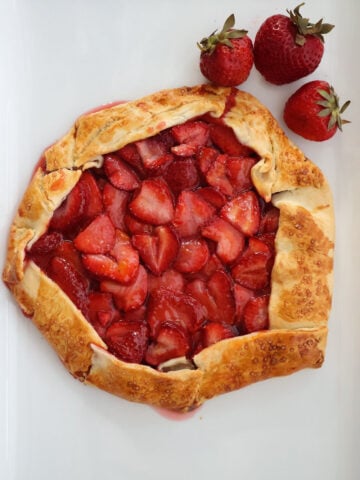 Freshly baked strawberry galette on white dish with strawberries on the side.