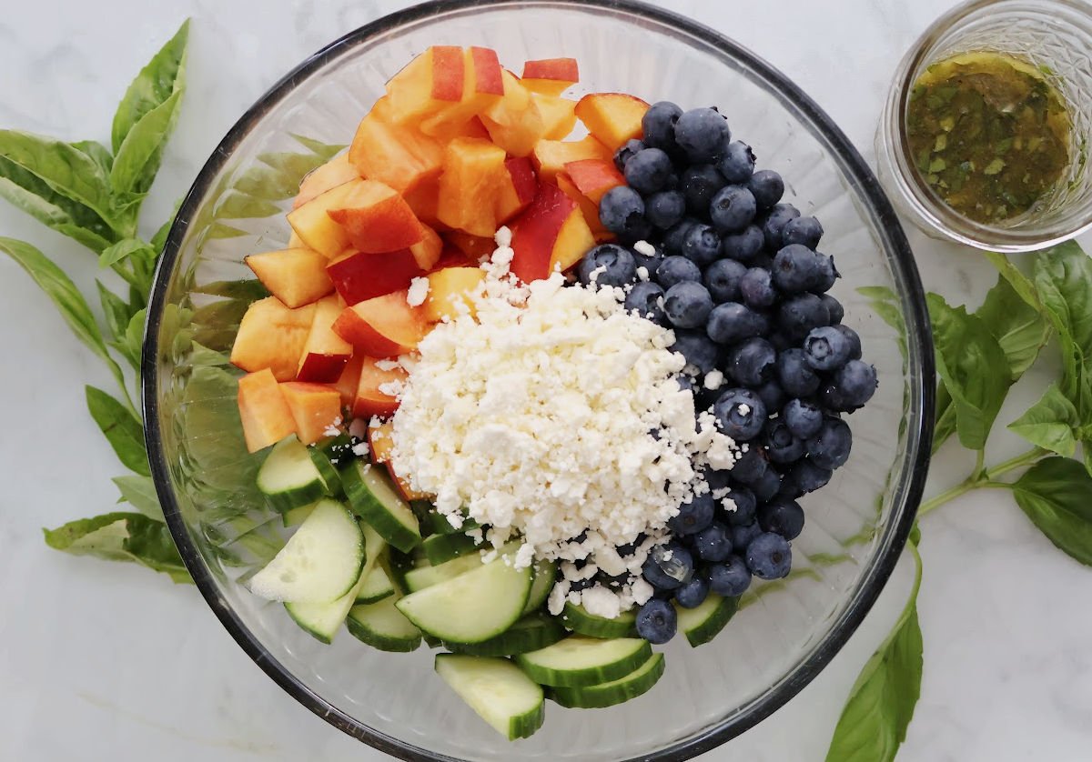 Blueberry Peach Feta Salad served in a white bowl with fresh basil garnish. Juicy peaches, blueberries, sliced cucumber, and crumbled feta are tossed in a light basil lemon vinaigrette. A fresh, colorful summer salad! 