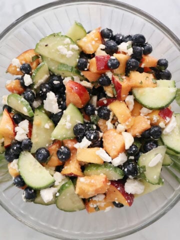 Blueberry Peach Feta Salad served in a glass bowl with fresh basil garnish. Juicy peaches, blueberries, sliced cucumber, and crumbled feta are tossed in a light basil lemon vinaigrette. A fresh, colorful summer salad that’s perfect for picnics or potlucks.