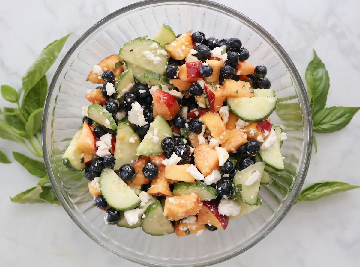 Blueberry Peach Feta Salad served in a glass bowl with fresh basil garnish. Juicy peaches, blueberries, sliced cucumber, and crumbled feta are tossed in a light basil lemon vinaigrette. A fresh, colorful summer salad that’s perfect for picnics or potlucks.