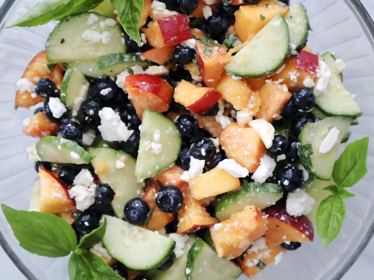 Blueberry Peach Feta Salad served in a white bowl with fresh basil garnish. Juicy peaches, blueberries, sliced cucumber, and crumbled feta are tossed in a light basil lemon vinaigrette. A fresh, colorful summer salad that’s perfect for picnics or potlucks.