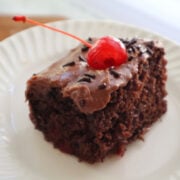 A piece of dr pepper cake with boiled icing garnished with a marachino cherry.