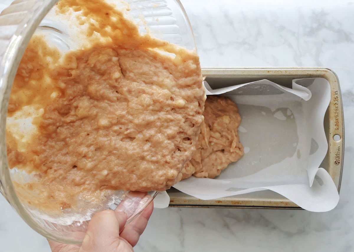 pouring homemade banana mix batter into a parchment lined loaf pan.