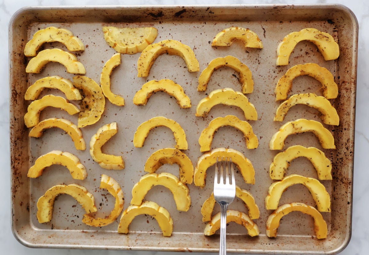 Half-moon slices of delicata squash arranged on baking sheet, seasoned and roasted. 