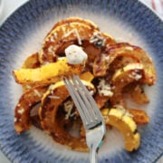 Delacata half moons, roasted and seasoned on a blue plate. A fork has a delicata fry on it that has been dipped in ranch dressing.