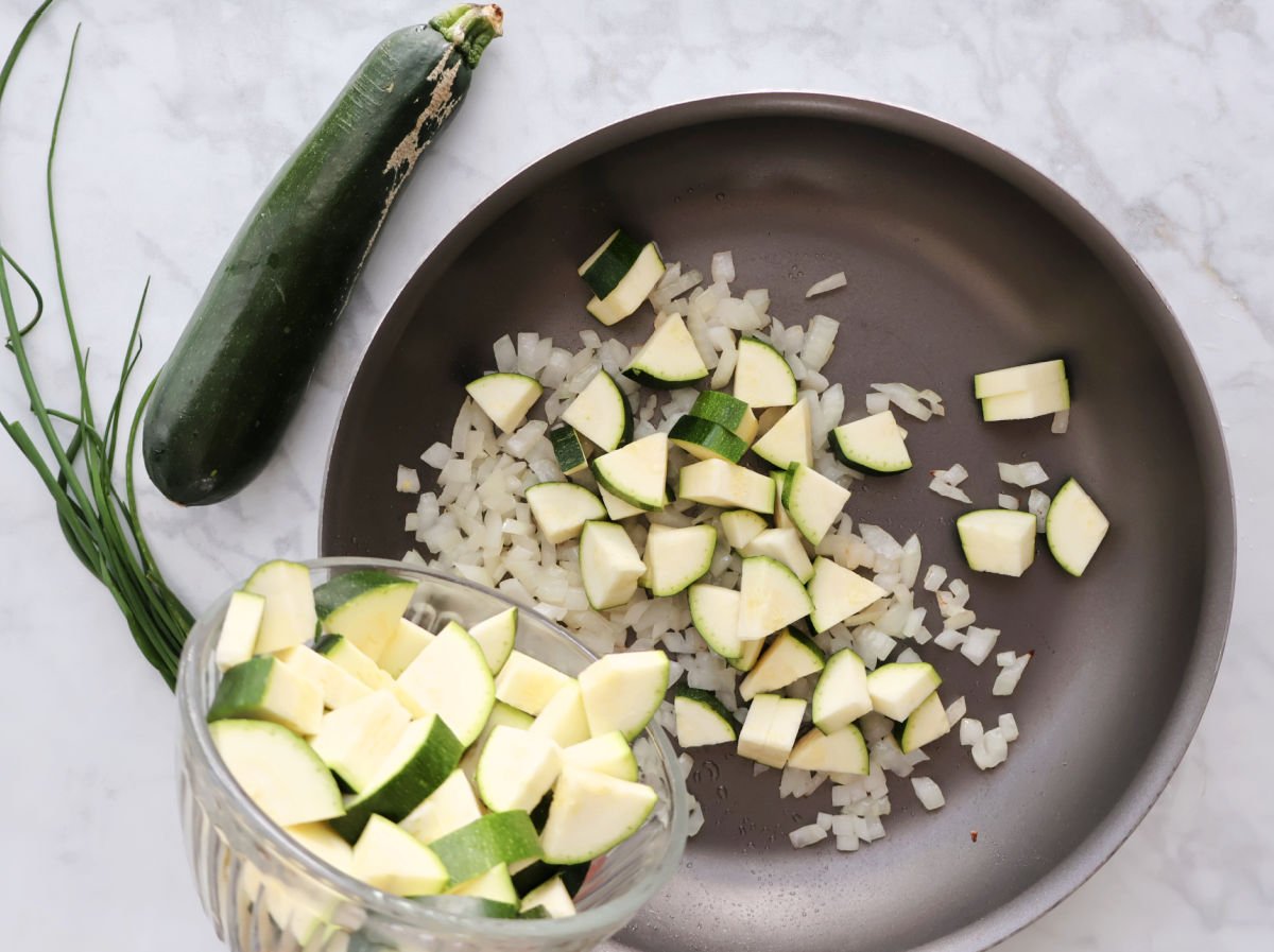 adding cubed zucchini to onions as part of the zucchini chicken and stuffing recipe.