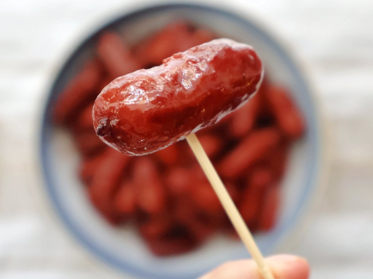 Cocktail sausages in sweet and tangy grape jelly chili sauce served in a white bowl with toothpicks.