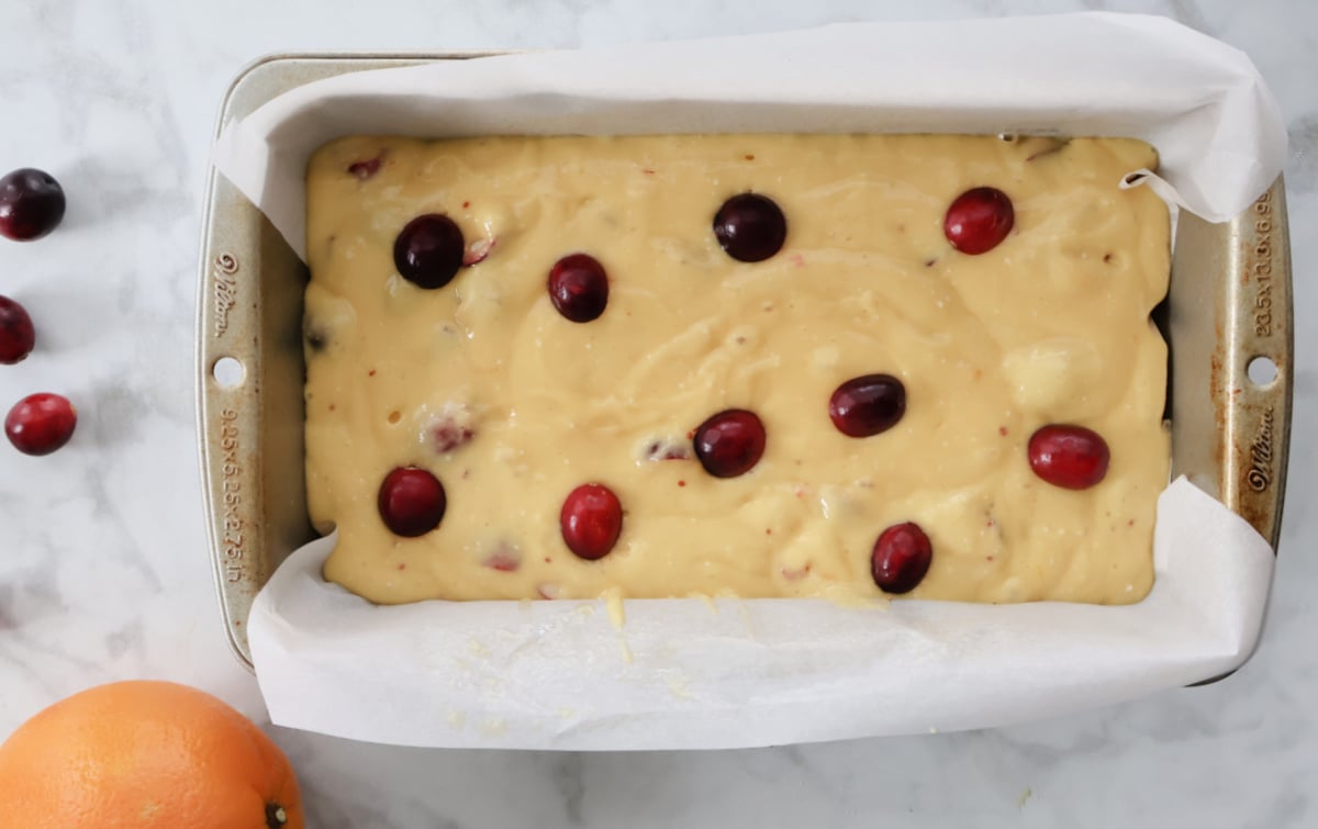 Cranberry orange bread ready for the oven in a loaf tin. Halved cranberries placed on top to decorate.