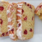Slice of cranberry orange bread on a white plate showing tart cranberries and bright orange glaze drizzled on a few slices
