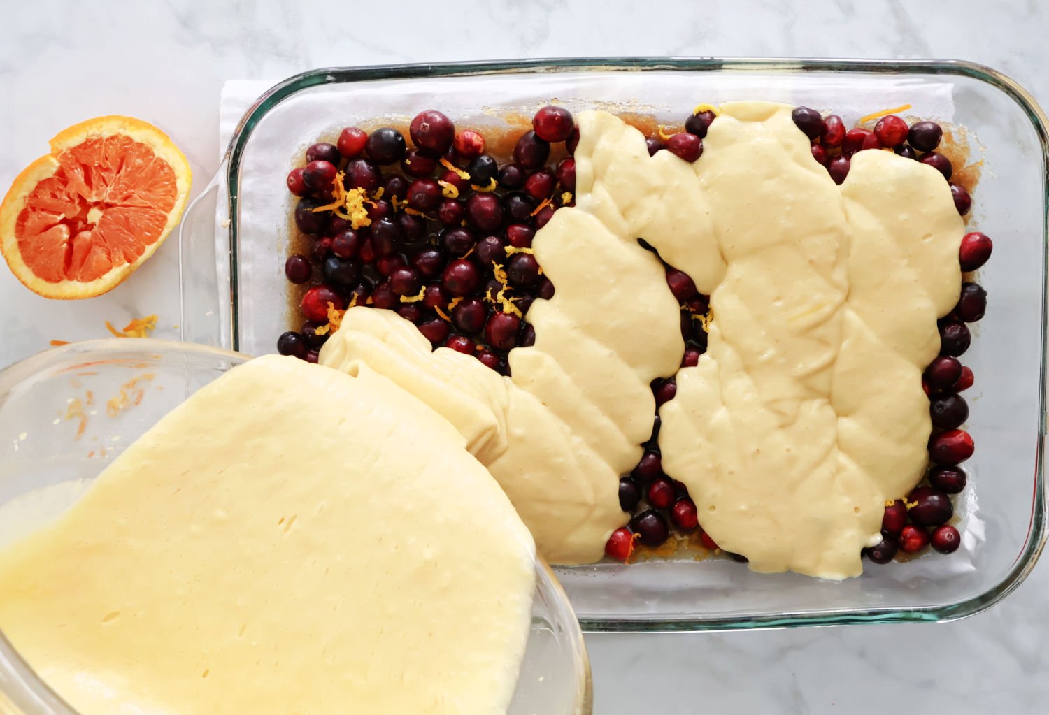 Cake batter being poured evenly over cranberry and orange layer in a 9x13 pan.