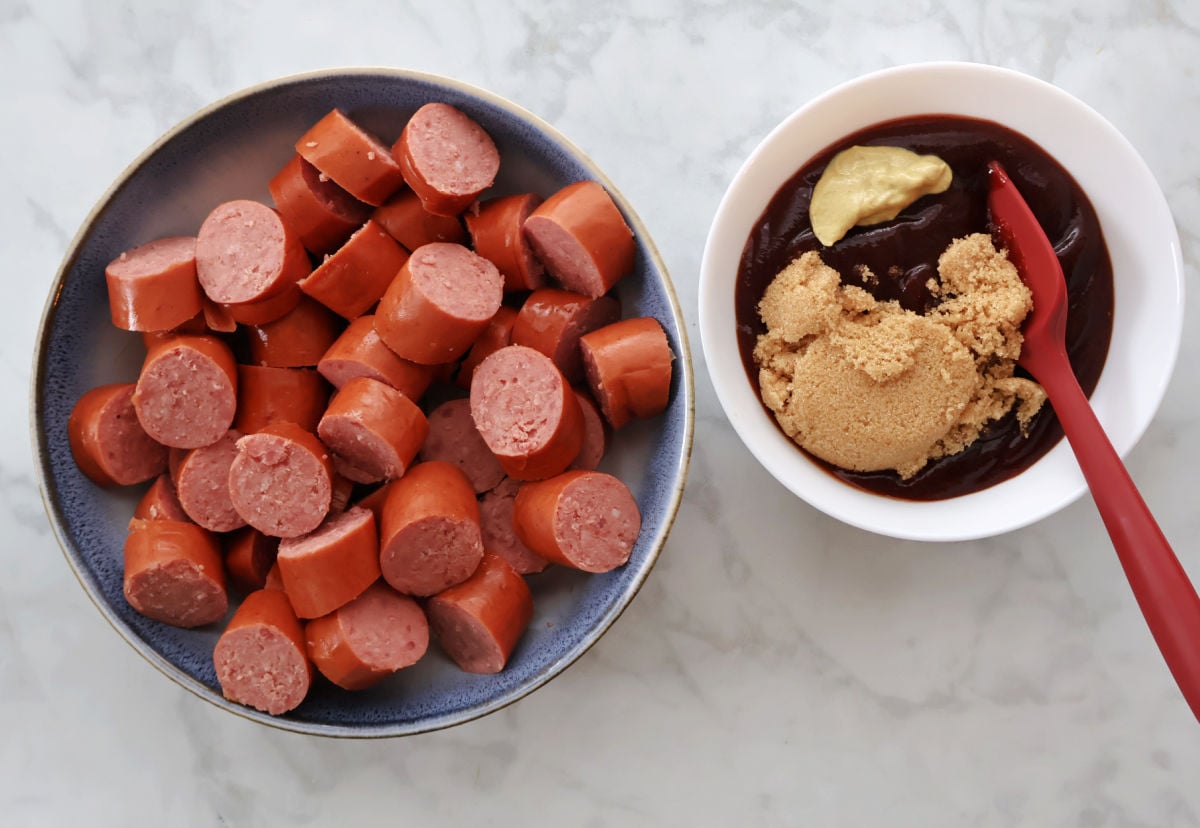  Barbecue sauce and brown sugar mixture being poured over sliced kielbasa in a slow cooker.