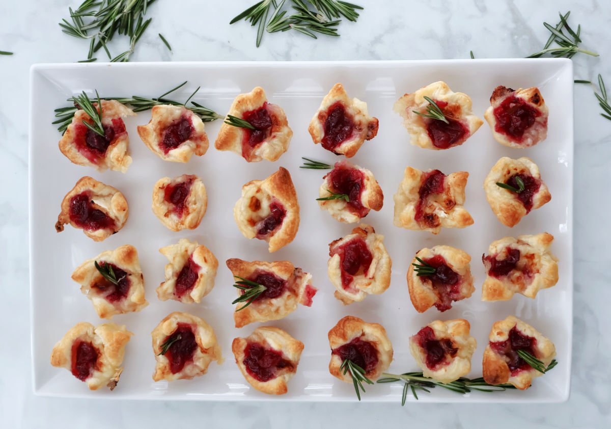 cranberry brie bites displayed on a white tray with rosemary garnish on the tray.