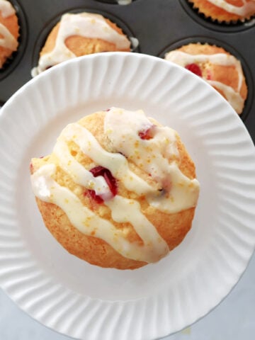 Cranberry orange muffin with orange drizzle. Muffin tin full of muffins in the background.
