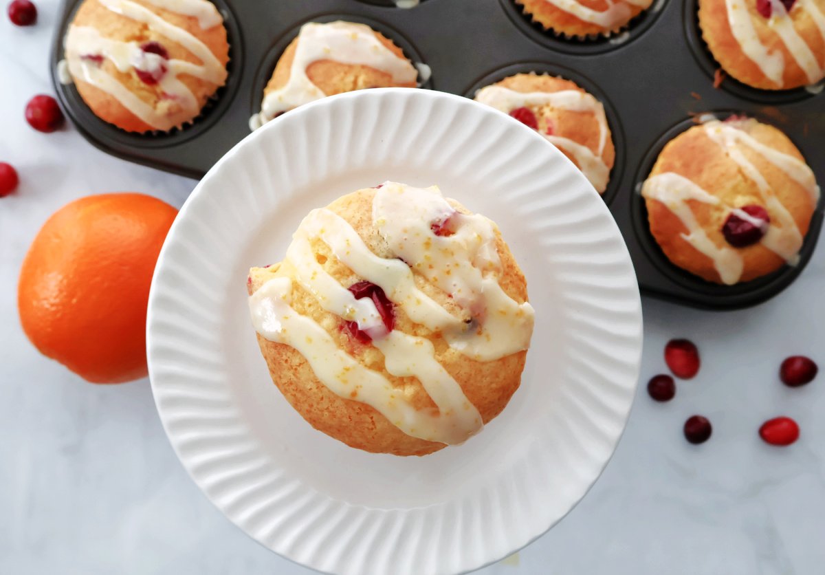 Cranberry orange muffin with orange drizzle. Muffin tin full of muffins in the background.
