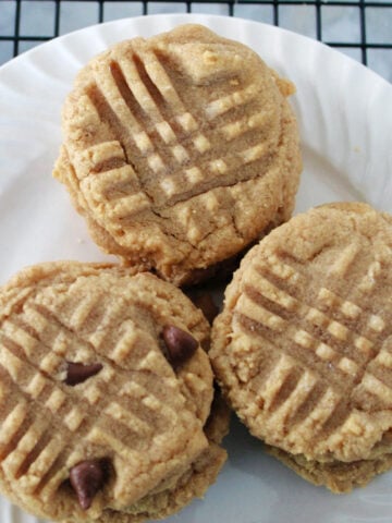 Close up of soft 3 ingredient peanut butter cookies with fork marks on top on a white plate.