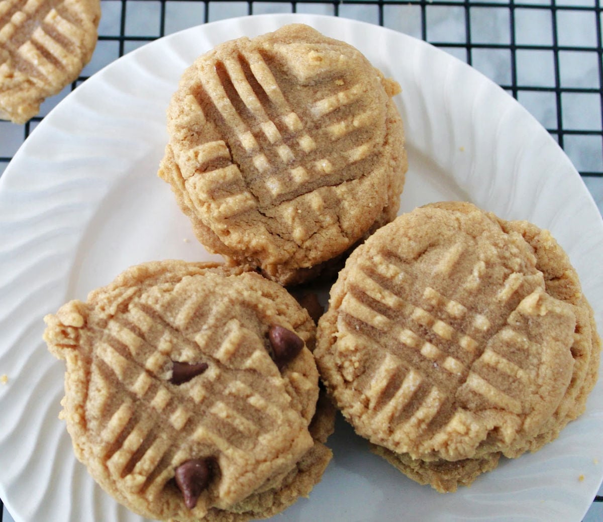 Close up of soft 3 ingredient peanut butter cookies with fork marks on top on a white plate.