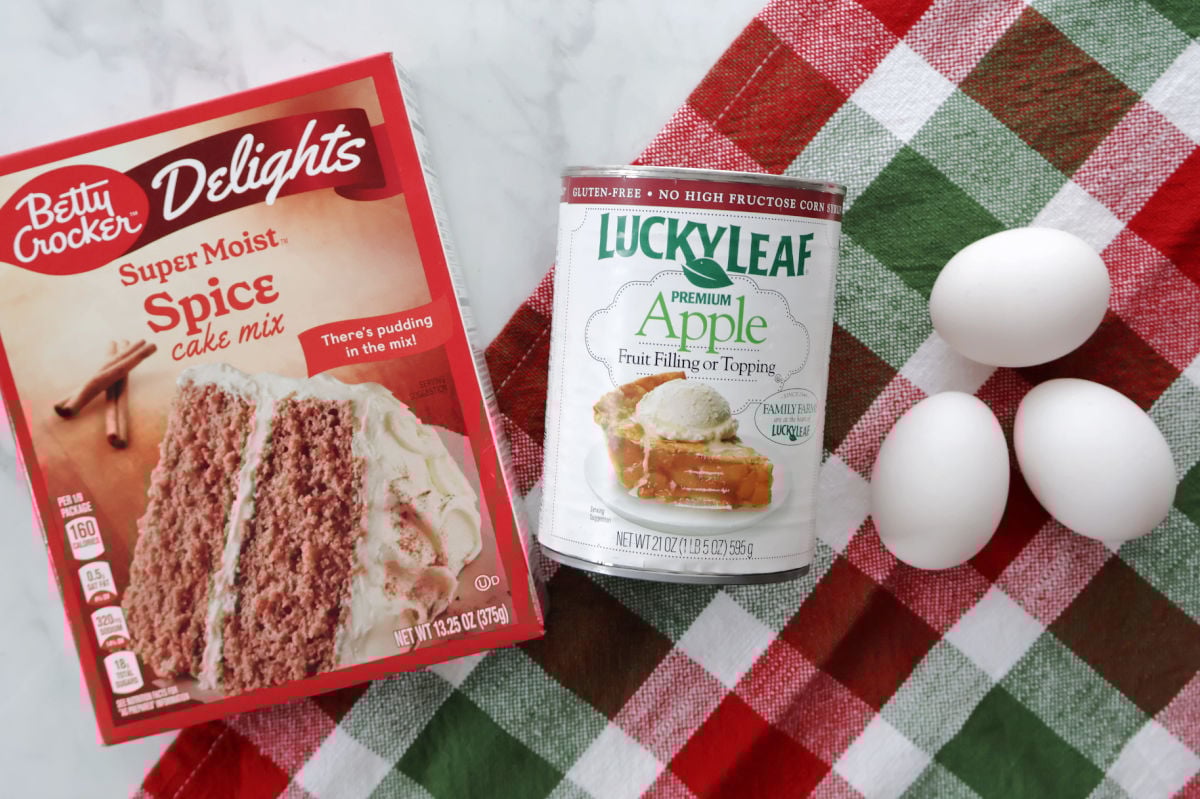 Three ingredients for Are You Kidding Me Cake: spice cake mix, apple pie filling, and eggs on a kitchen counter.