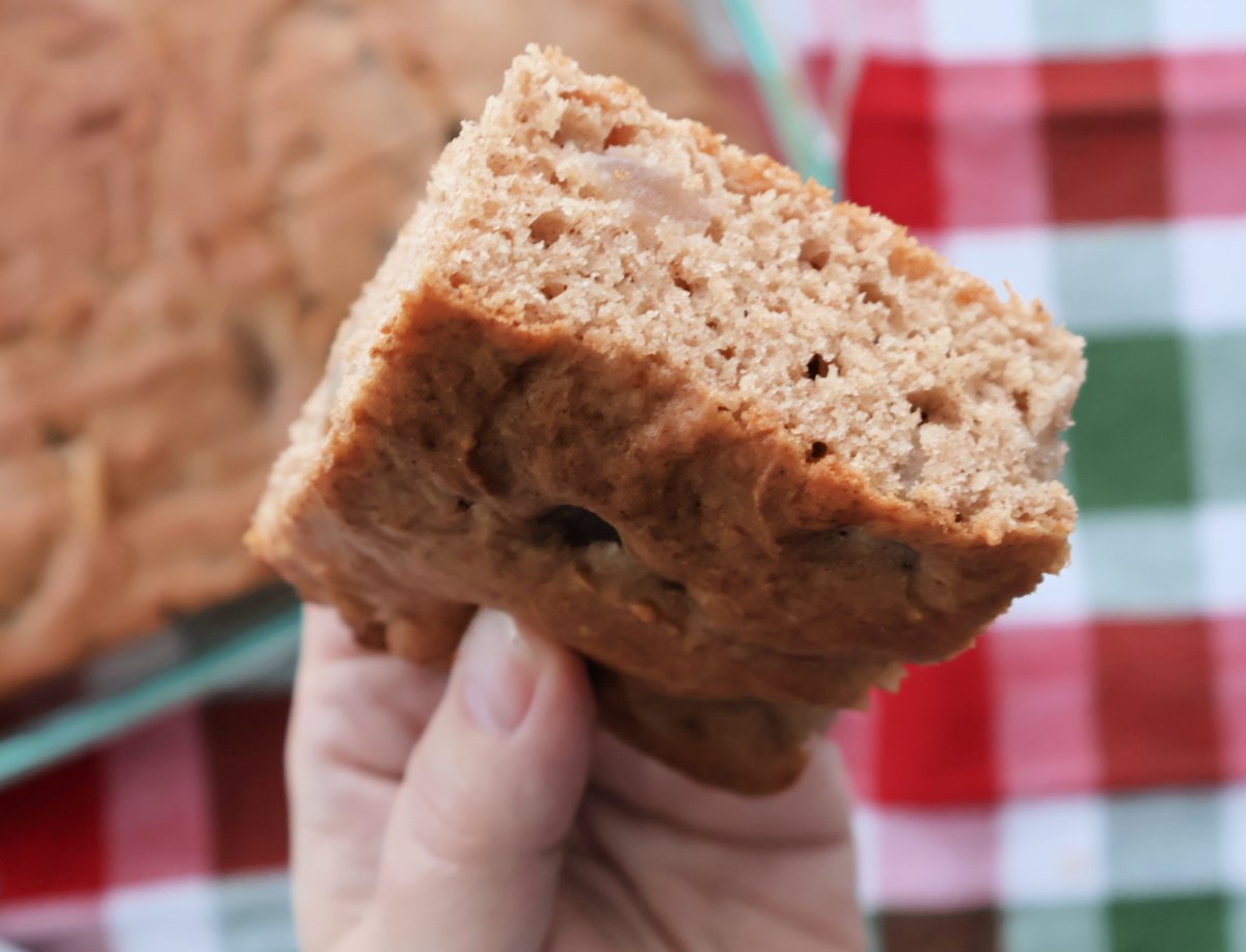 Slice of apple spice cake made with spice cake mix and apple pie filling above the baking pan full of freshly baked are you kidding me cake.